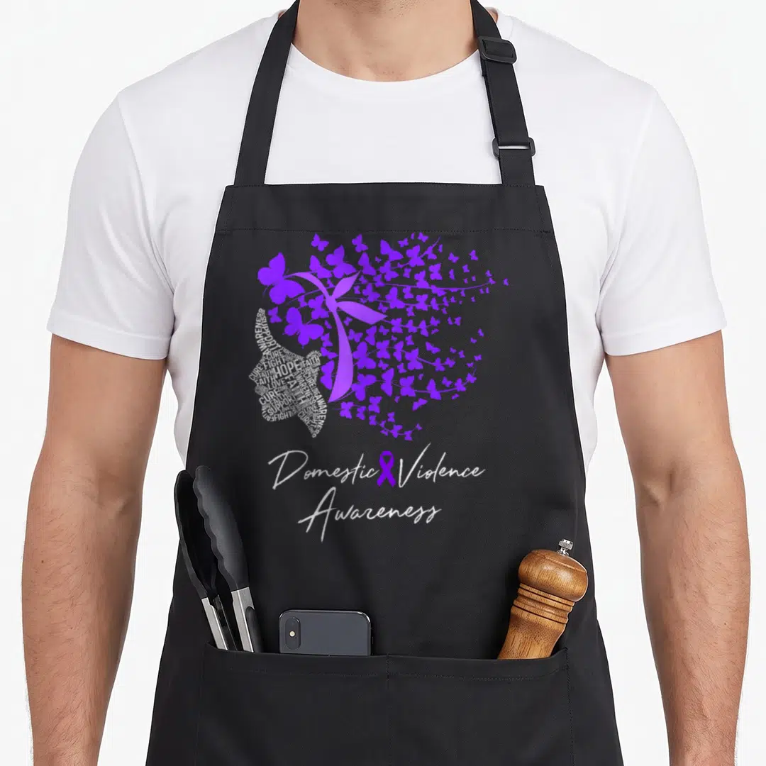 Awareness domestic aprons - Woman profile made of white text with purple butterflies and ribbon below — shown on a black cotton canvas apron against a white background
