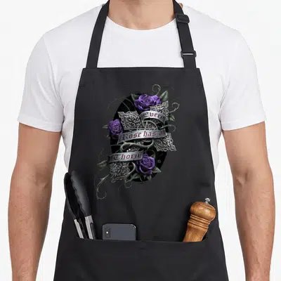 Spiral rose apron - Three purple roses and thorns around silver banners reading Every Rose has a Thorn — shown on a black cotton canvas apron against a white background