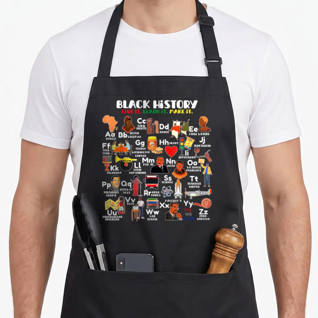 Abc teacher apron - Black history alphabet grid with cartoon illustrations of historical figures and symbols in red — shown on a black cotton canvas apron against a white background