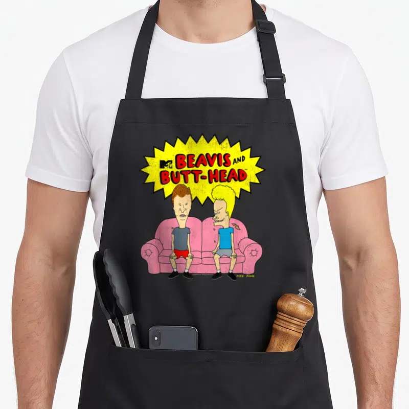Butt couch apron - Beavis and Butt-Head on pink sofa under yellow burst with red text and MTV logo — shown on a black cotton canvas apron against a white background