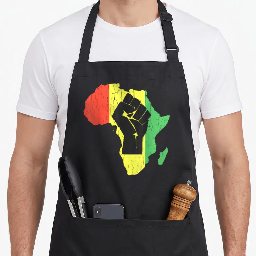 Power african apron - Black raised fist over Africa map with vertical red yellow green stripes in distressed style — shown on a black cotton canvas apron against a white background