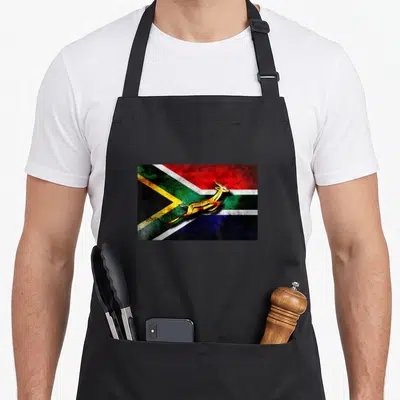 Springbok bokke south african apron - Rectangular flag with gold leaping springbok in red blue green yellow white black — shown on a black cotton canvas apron against a white background