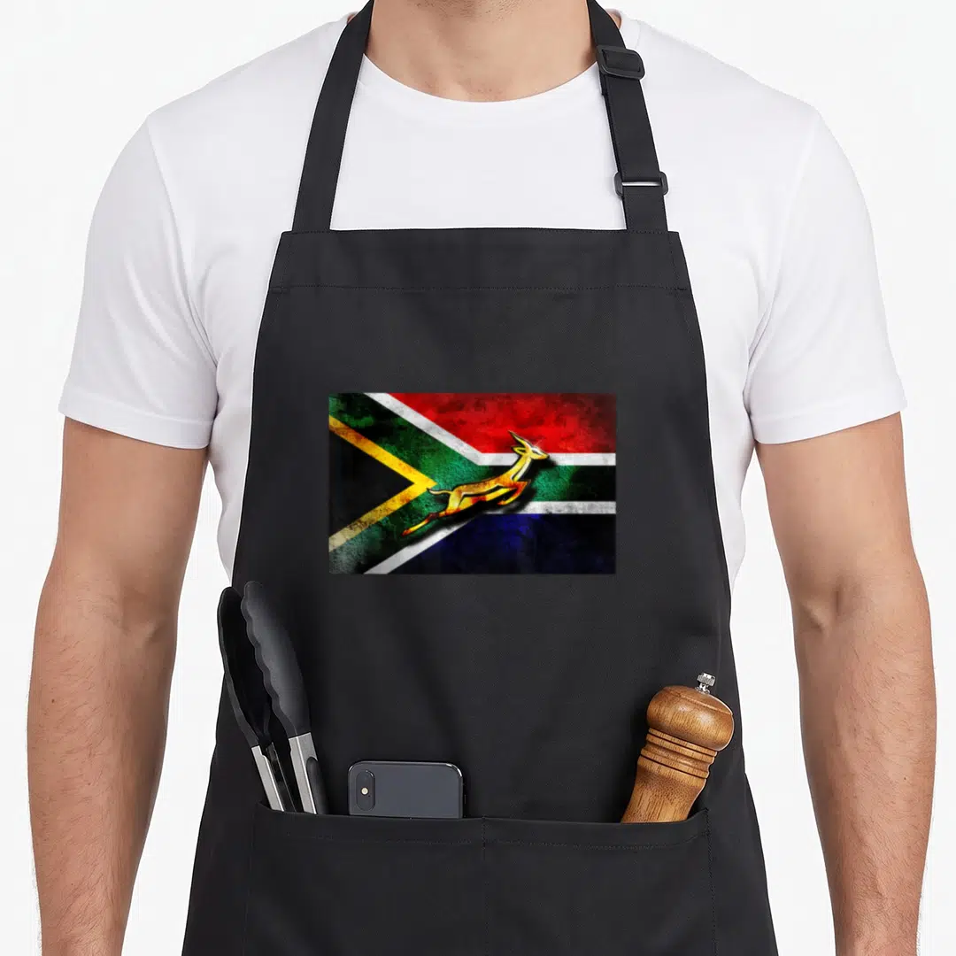 Springbok bokke south african apron - Rectangular flag with gold leaping springbok in red blue green yellow white black — shown on a black cotton canvas apron against a white background