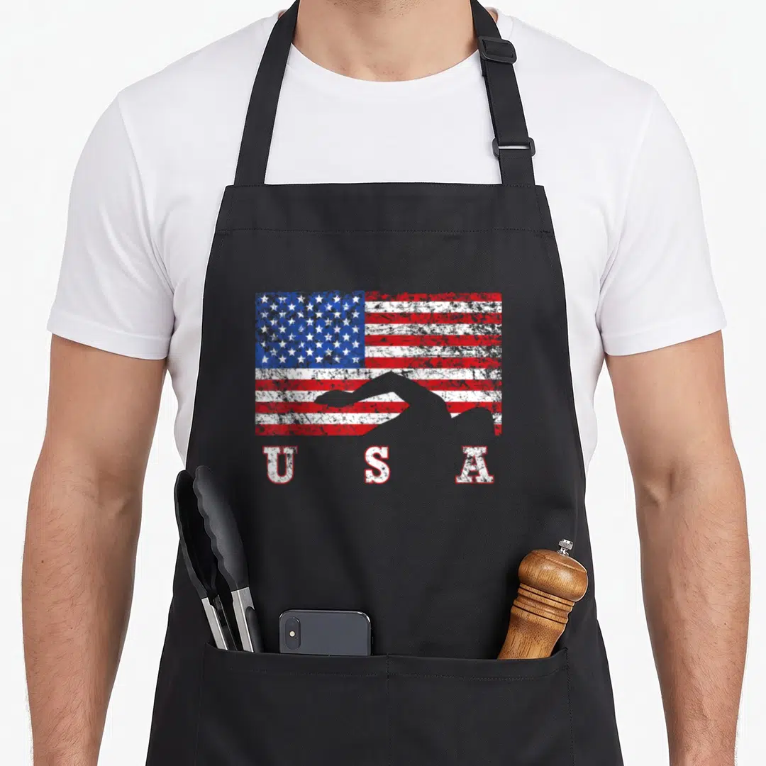 Swimming american flag apron - Distressed USA flag with grey swimmer silhouette and U S A text below — shown on a black cotton canvas apron against a white background