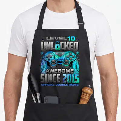 Unlocked gaming aprons - Level 10 Unlocked controller with stars and since 2015 text — shown on a black cotton canvas apron against a white background