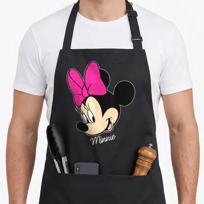 Friend face apron - Cartoon Minnie Mouse head with pink bow and white Minnie text on black background — shown on a black cotton canvas apron against a white background