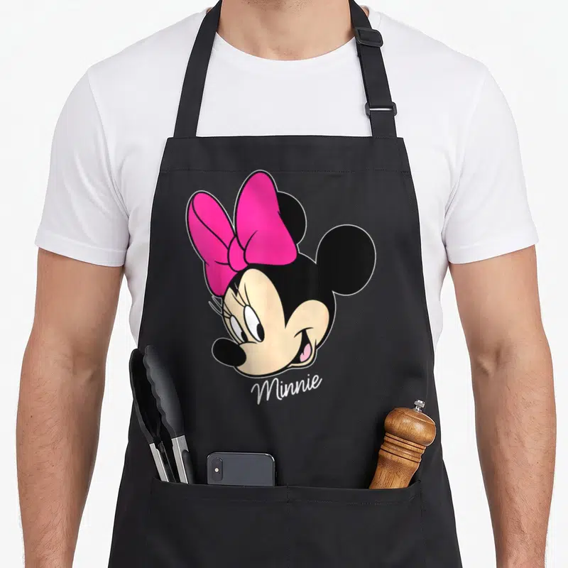 Friend face apron - Cartoon Minnie Mouse head with pink bow and white Minnie text on black background — shown on a black cotton canvas apron against a white background