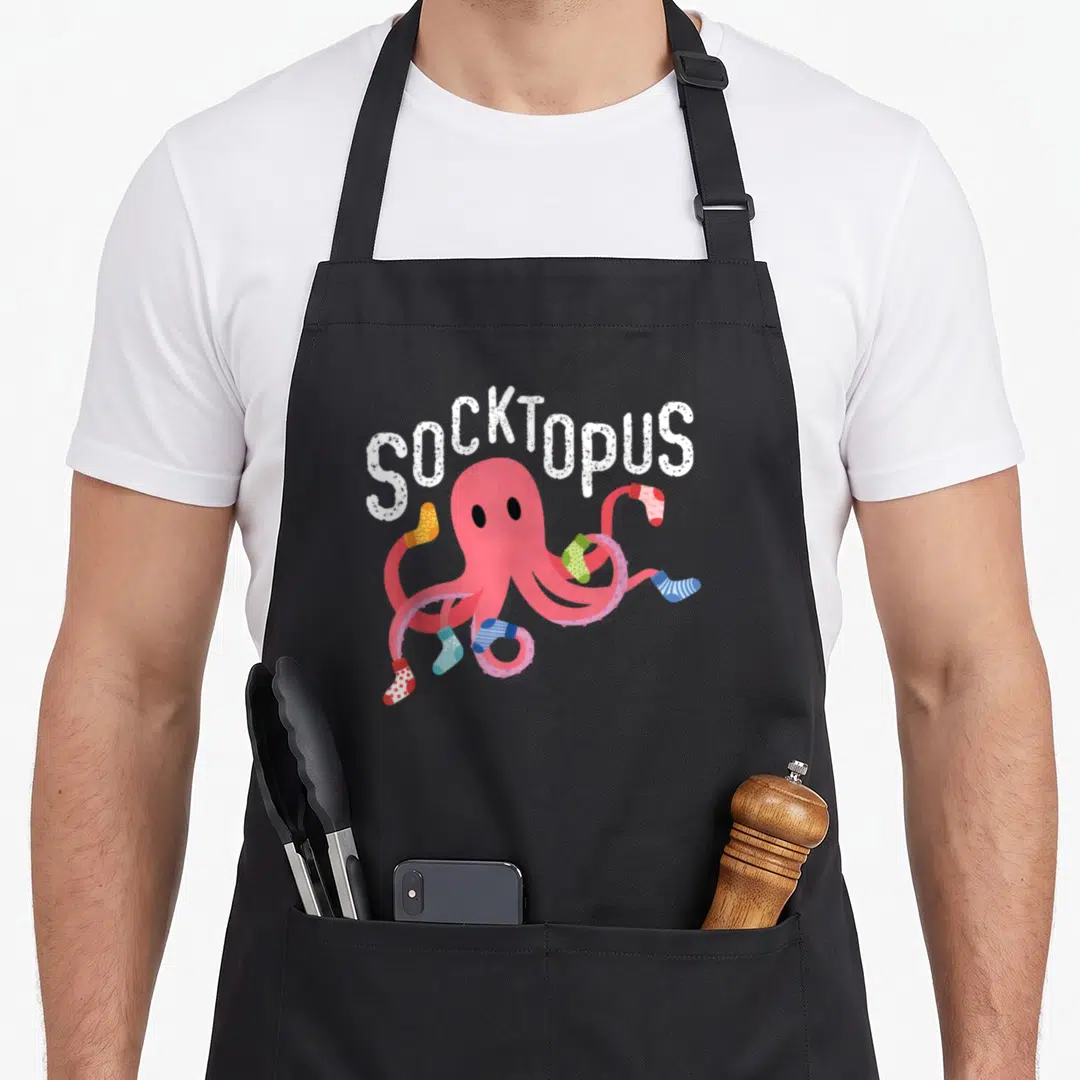 Socktopus quirky apron - Pink octopus wearing colorful socks under arched white SOCKTOPUS text — shown on a black cotton canvas apron against a white background