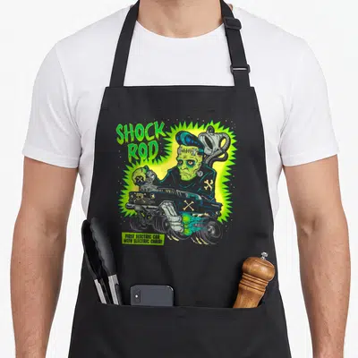 Frankenstein horror apron - Green monster behind grey gasser with SHOCK ROD text and jagged yellow glow — shown on a black cotton canvas apron against a white background