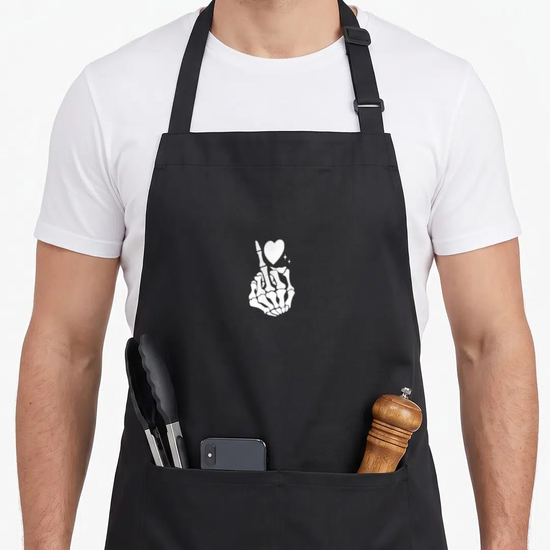 Groovy skeleton apron - White skeletal hand pointing up with heart and two sparkles — shown on a black cotton canvas apron against a white background