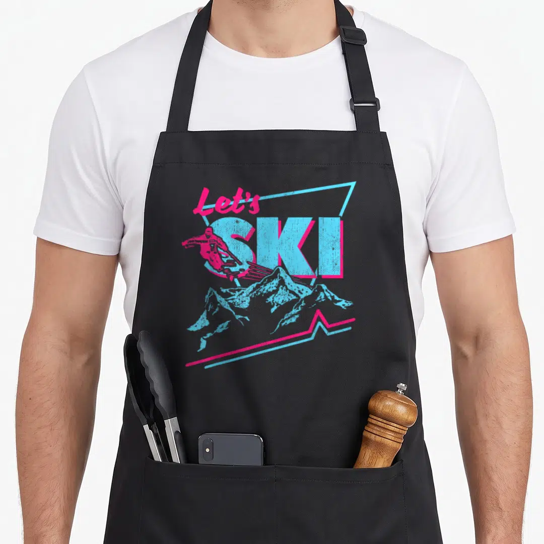 Outfit 80s apron - Retro Let's SKI text with pink skier overlapping S and blue mountains — shown on a black cotton canvas apron against a white background