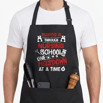 Making nursing student apron - Red and white stacked text reading making it through nursing school one meltdown — shown on a black cotton canvas apron against a white background