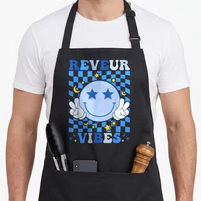 Reveur face apron - Blue smiley with star eyes and peace hands over wavy checkerboard with REVEUR VIBES text — shown on a black cotton canvas apron against a white background