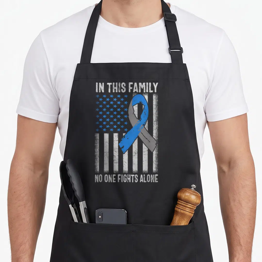 Flag family aprons - Blue ribbon over distressed US flag with text IN THIS FAMILY NO ONE FIGHTS ALONE — shown on a black cotton canvas apron against a white background