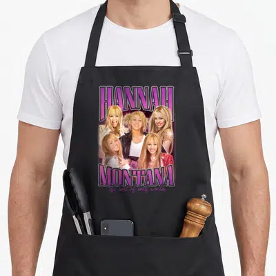 Popstar montana girl apron - Five blonde woman photos between purple HANNAH and MONTANA text with cursive tagline — shown on a black cotton canvas apron against a white background