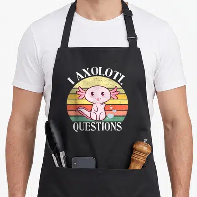 Question axolotl funny apron - Pink cartoon axolotl in front of striped sun with I Axolotl Questions text and small — shown on a black cotton canvas apron against a white background