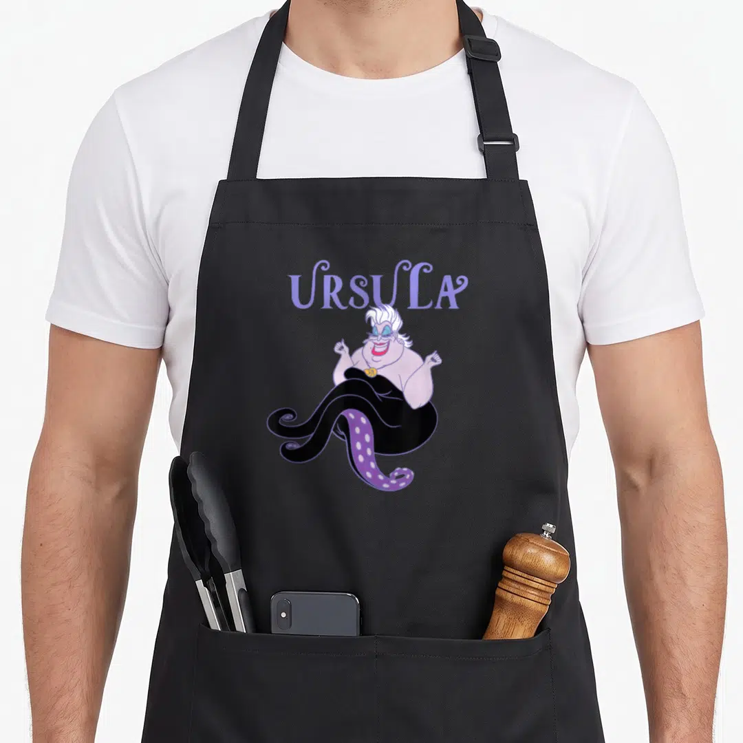 Villain mermaid apron - Ursula text above cartoon sea witch with purple tentacles and black lower body — shown on a black cotton canvas apron against a white background