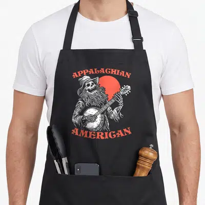 Appalachian skeleton apron - White line-art skeleton playing banjo in front of red sun with APPALAGHIAN AMERICAN text — shown on a black cotton canvas apron against a white background