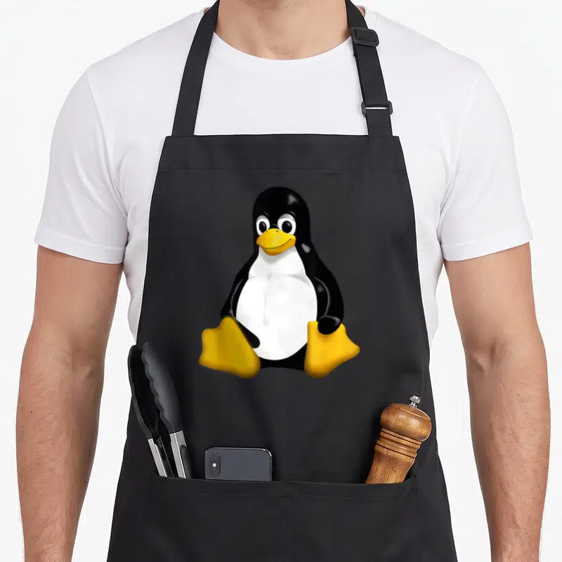 Tux linux penguin aprons - Cartoon penguin in black white and yellow centered on canvas — shown on a black cotton canvas apron against a white background