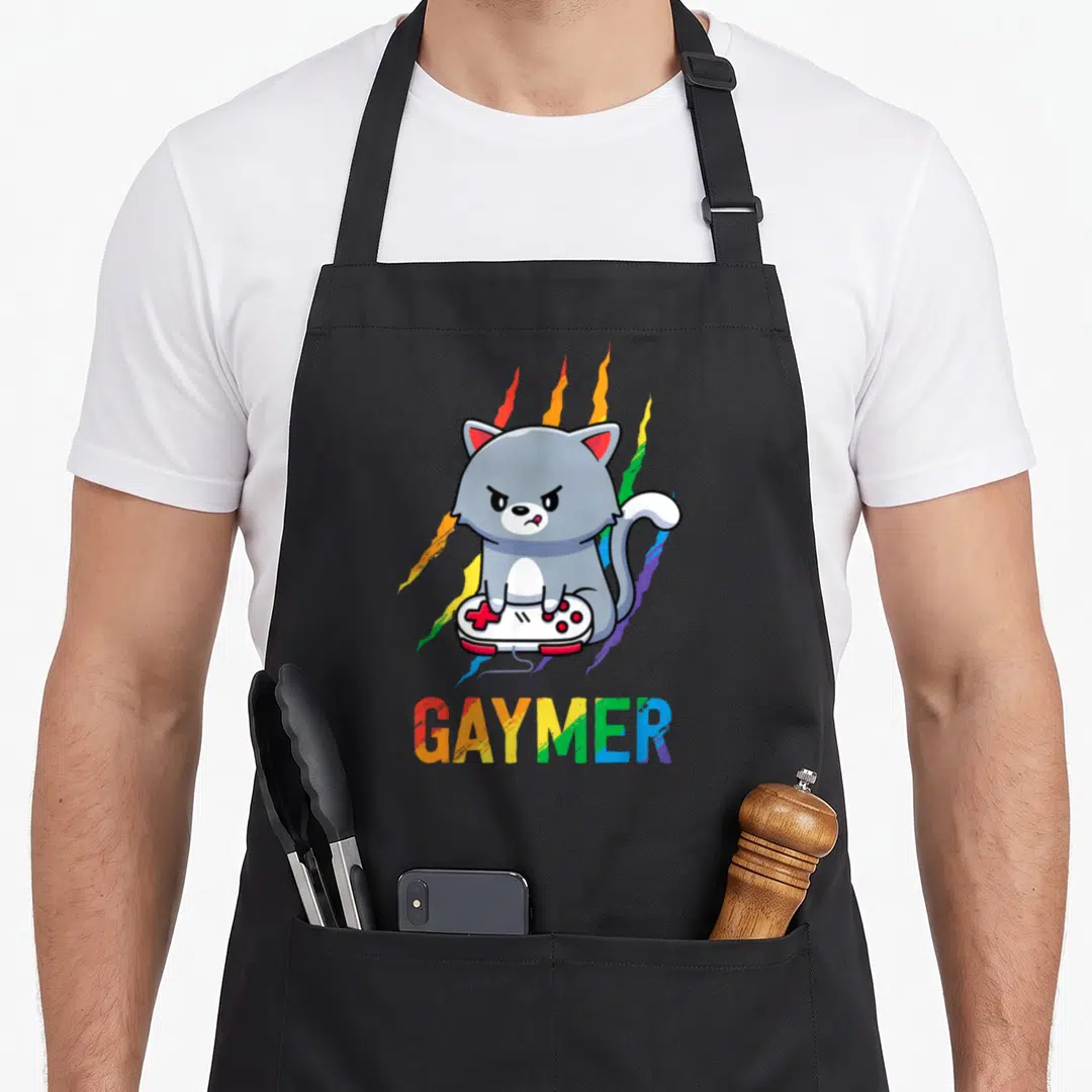 Gaymer video game apron - Grumpy grey cat on white controller with rainbow streaks and GAYMER text below — shown on a black cotton canvas apron against a white background