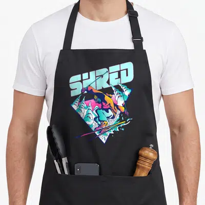 Shred 80s apron - Cartoon skier in triangle frame with SHRED text in blue pink purple yellow — shown on a black cotton canvas apron against a white background