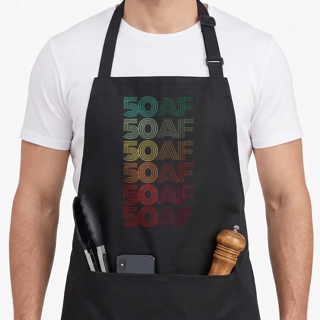 50th hello fifty birthday apron - Six stacked lines of 50AF text in teal, olive, gold, orange, and red — shown on a black cotton canvas apron against a white background