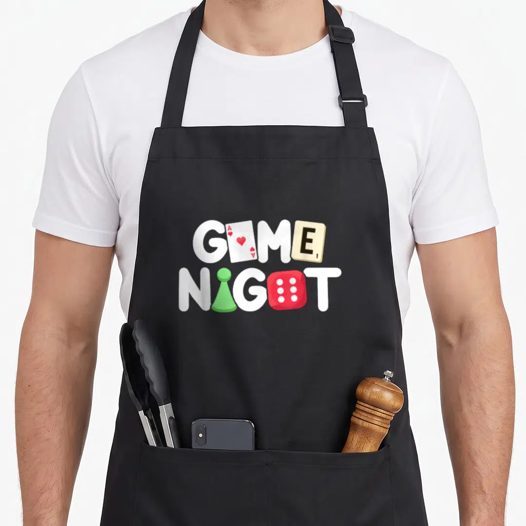 Host game aprons - Stacked GAME NIGHT text with Ace card, Scrabble tile, green pawn and red die replacing letters — shown on a black cotton canvas apron against a white background