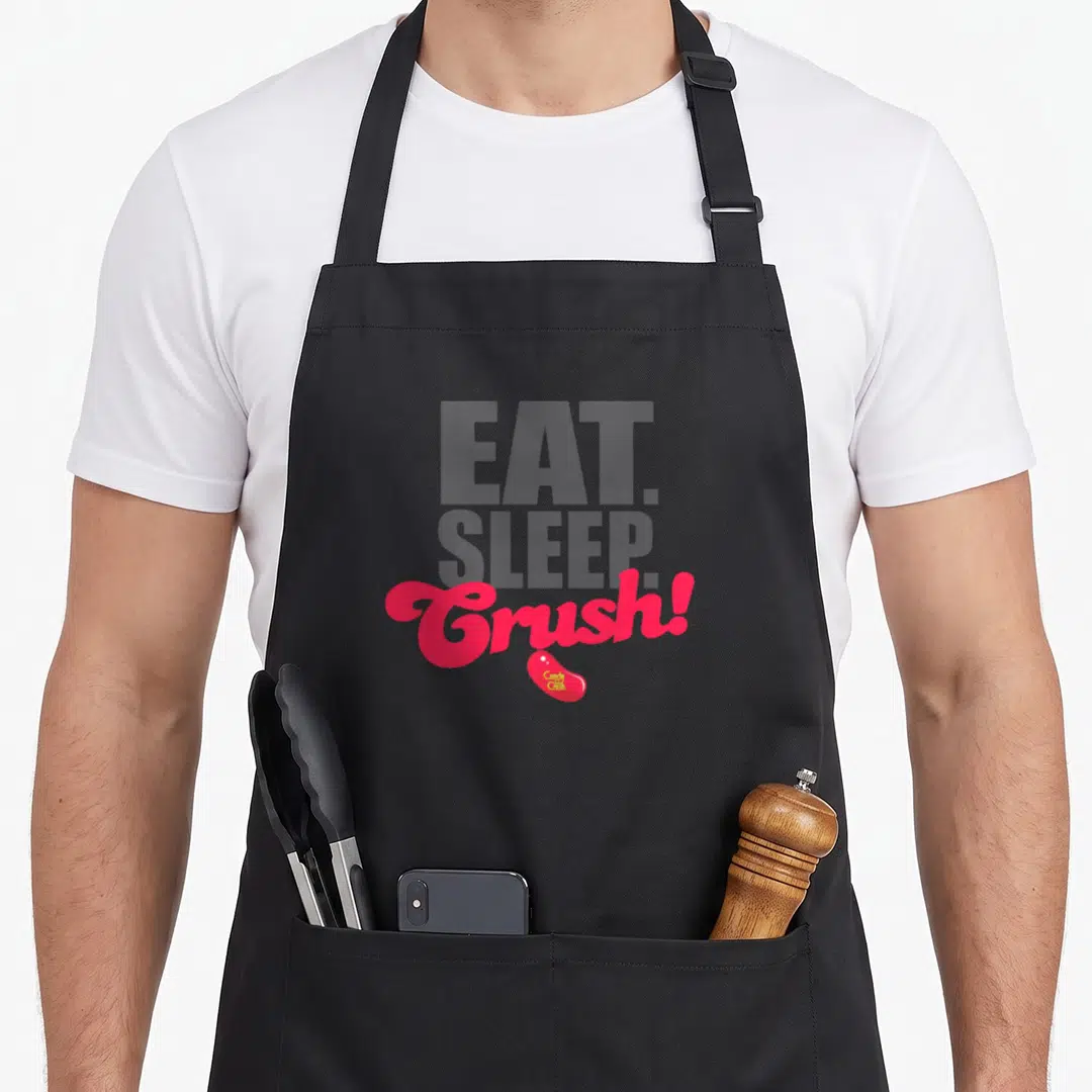 Eat sleep apron - Stacked EAT SLEEP Crush text with pink script and red candy graphic on grey background — shown on a black cotton canvas apron against a white background