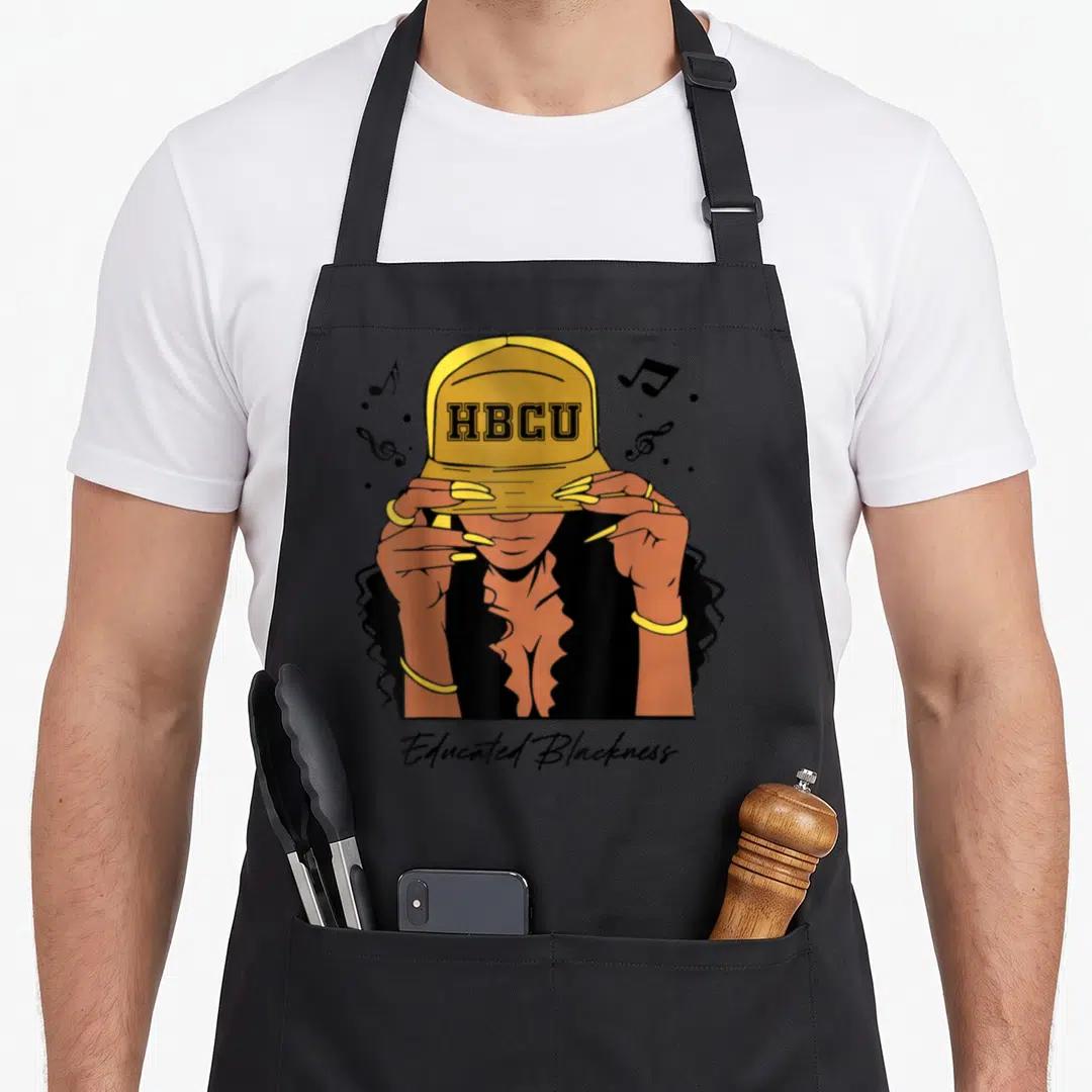 Historically college apron - Cartoon woman in yellow HBCU cap surrounded by notes with Educated Blackness text below — shown on a black cotton canvas apron against a white background