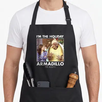 Ross holiday apron - I'M THE HOLIDAY ARMADILLO text framing photo of two people in white border with tan and purple — shown on a black cotton canvas apron against a white background