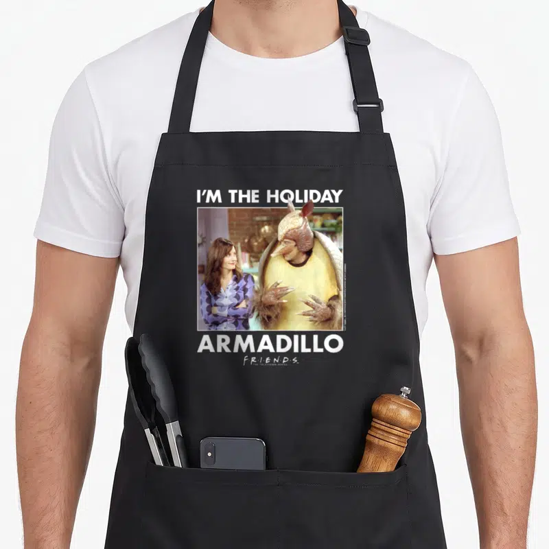 Ross holiday apron - I'M THE HOLIDAY ARMADILLO text framing photo of two people in white border with tan and purple — shown on a black cotton canvas apron against a white background