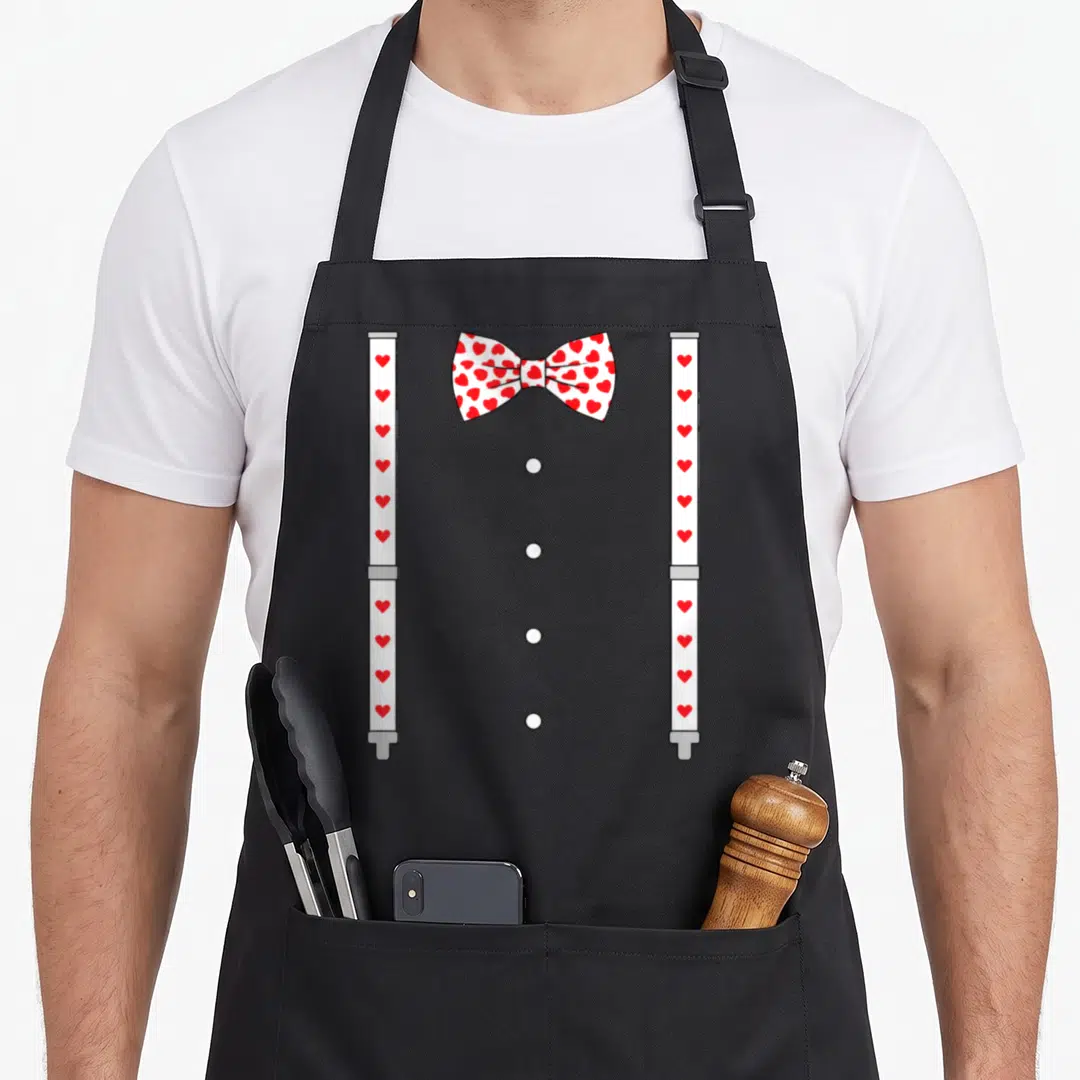 Suspender bow apron - White bow tie with red hearts and matching suspenders with four grey buttons — shown on a black cotton canvas apron against a white background