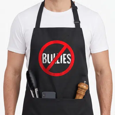 Bully teacher apron - Red prohibition circle with white distressed BULLIES text and diagonal slash — shown on a black cotton canvas apron against a white background