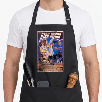 Funny movie poster apron - Retro Star Wars poster with Luke Skywalker, Death Star, and actor names in blue and yellow — shown on a black cotton canvas apron against a white background