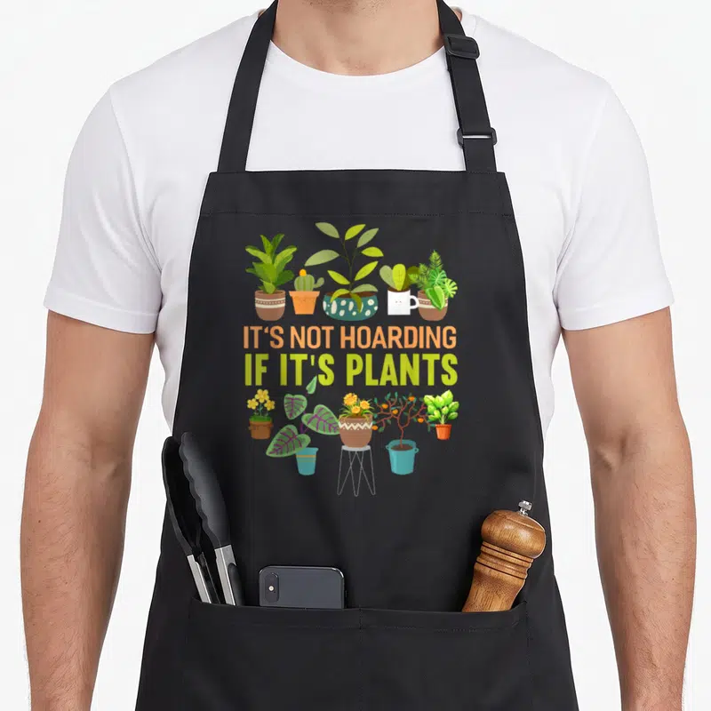 Hoarding plant apron - Five potted plants above text, six below including one on stand, cartoon style — shown on a black cotton canvas apron against a white background