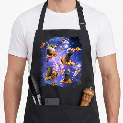 Space pizza apron - Four capybaras riding pizza slices in blue space with burritos and lollipop — shown on a black cotton canvas apron against a white background