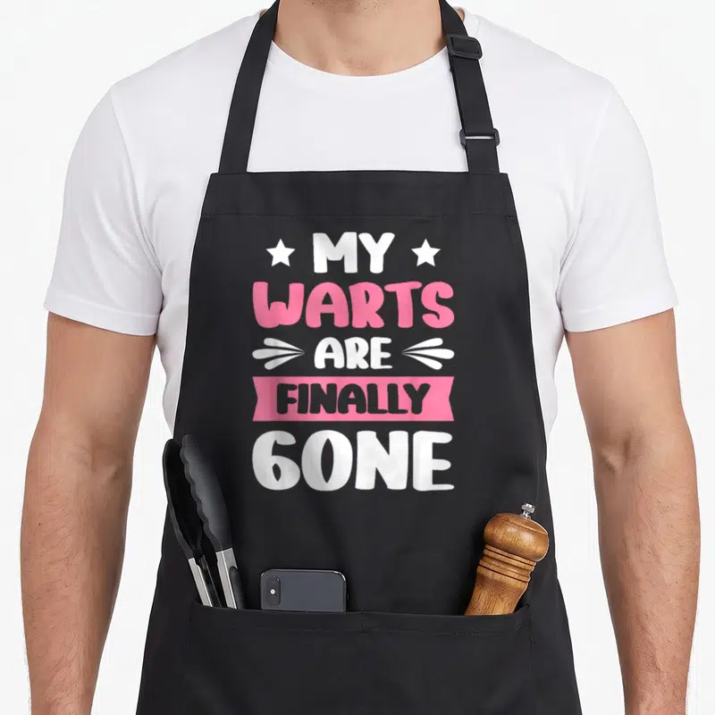 Finally funny wart apron - White and pink stacked text reading MY WARTS ARE FINALLY GONE with stars and banner graphics — shown on a black cotton canvas apron against a white background
