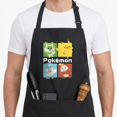 Pok group shot apron - Four cartoon Pokémon in colored squares with central white and black text logo — shown on a black cotton canvas apron against a white background