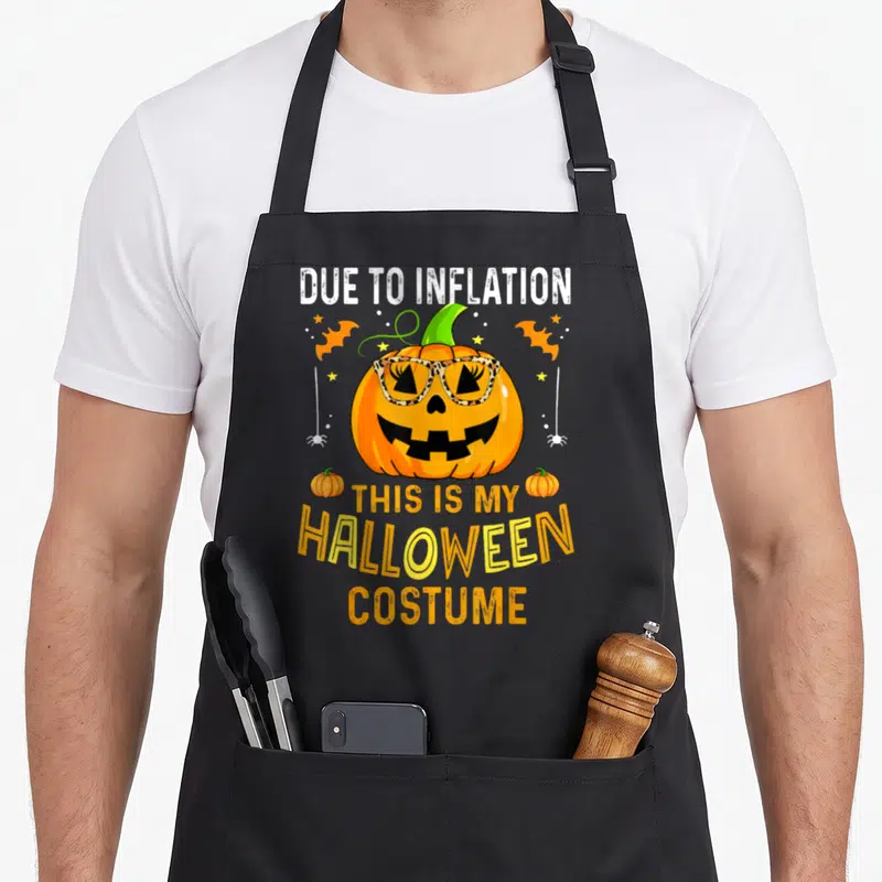 Costume pumpkin apron - Pumpkin wearing leopard print glasses with text about inflation and Halloween costume sarcasm — shown on a black cotton canvas apron against a white background