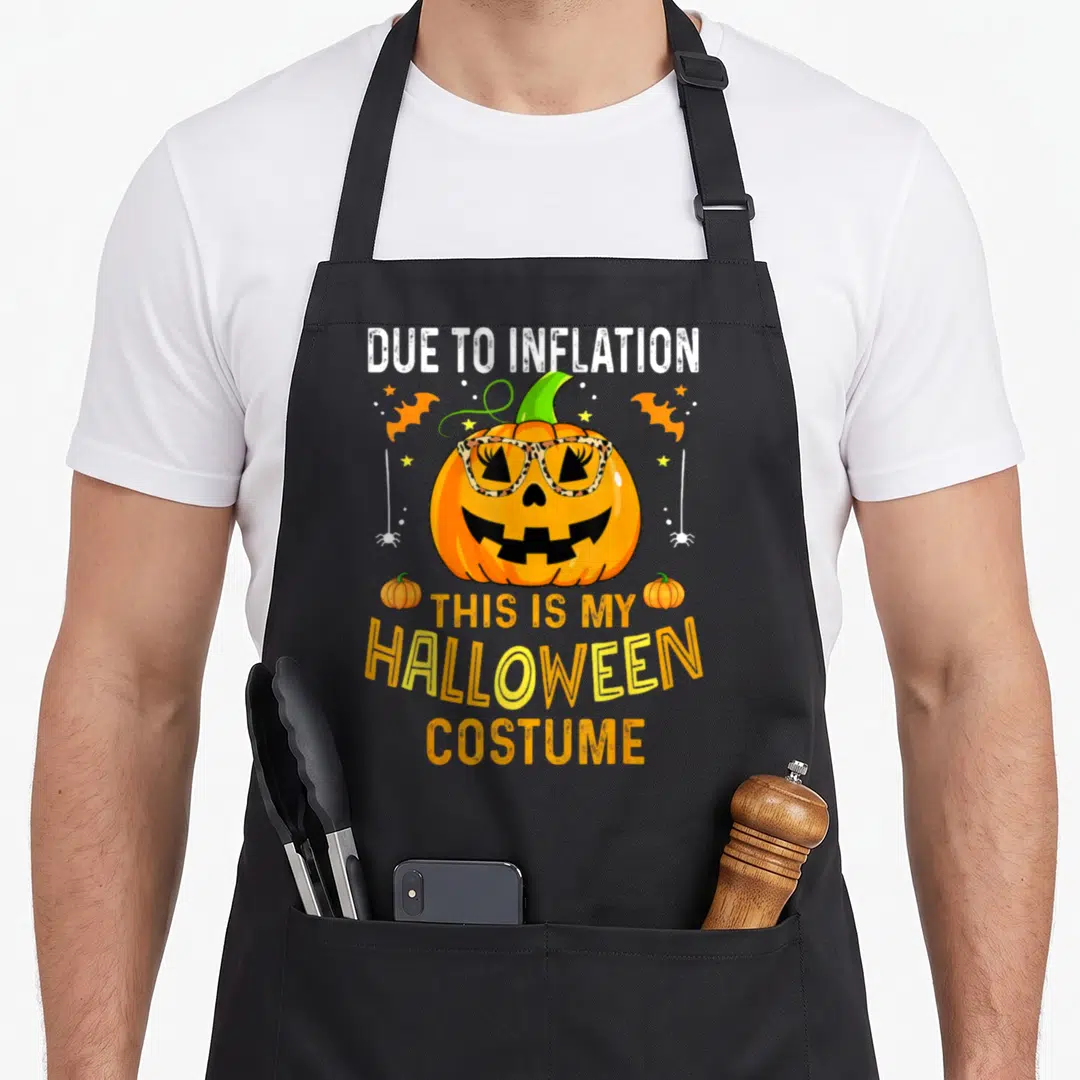 Costume pumpkin apron - Pumpkin wearing leopard print glasses with text about inflation and Halloween costume sarcasm — shown on a black cotton canvas apron against a white background