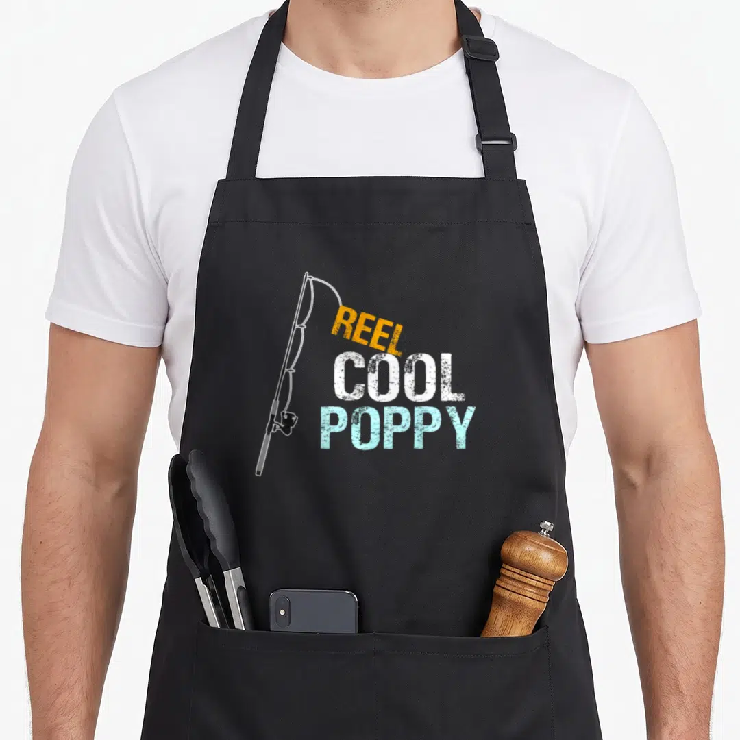 Reel grandpa apron - Fishing rod next to stacked text reading REEL COOL POPPY — shown on a black cotton canvas apron against a white background