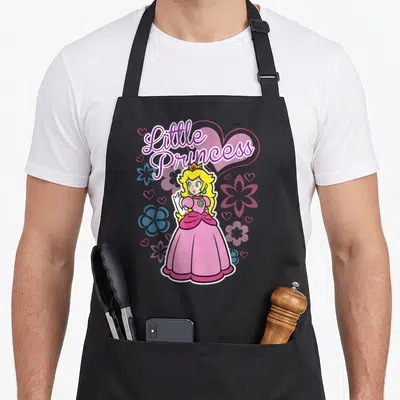 Peach flower princess apron - Little Princess text above Princess Peach in pink dress with blue and purple flowers — shown on a black cotton canvas apron against a white background