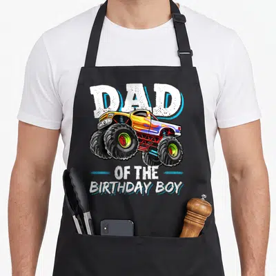 Birthday monster truck aprons - Cartoon monster truck with Dad of the Birthday Boy text in white and blue — shown on a black cotton canvas apron against a white background