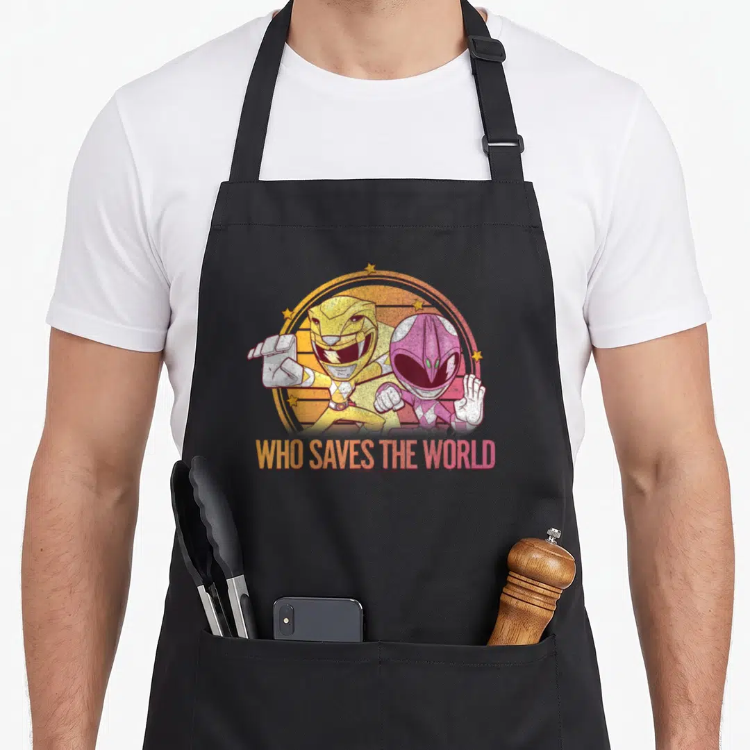 Save rangers apron - Two Power Rangers in yellow and pink inside a starry circle with gradient text below — shown on a black cotton canvas apron against a white background