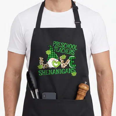 Shenanigan preschool apron - Gnome in plaid hat holding heart inside LOVE text with shamrocks — shown on a black cotton canvas apron against a white background