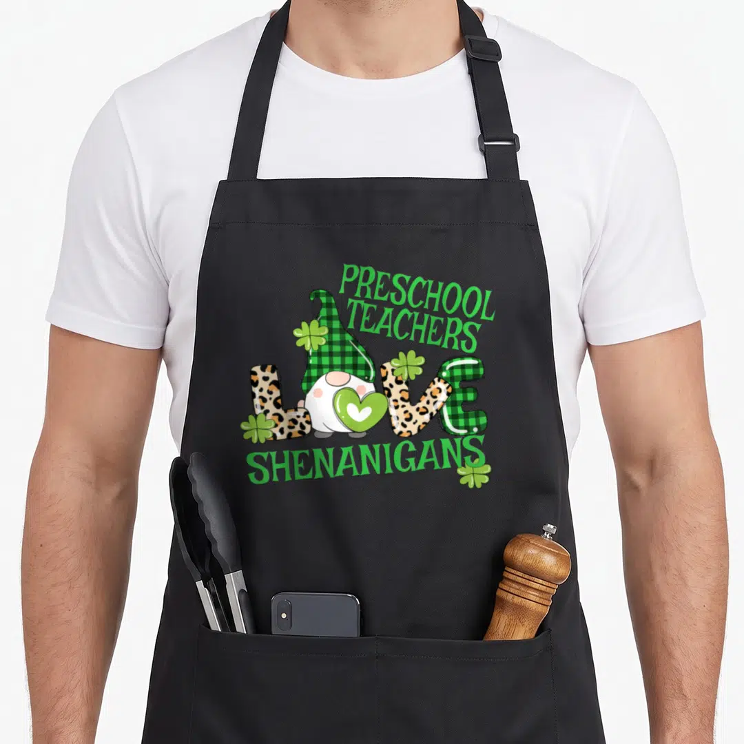 Shenanigan preschool apron - Gnome in plaid hat holding heart inside LOVE text with shamrocks — shown on a black cotton canvas apron against a white background