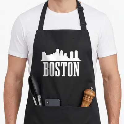 Massachusett pride apron - White silhouette of Boston skyline above the word BOSTON in bold capital letters — shown on a black cotton canvas apron against a white background