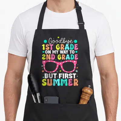 1st summer aprons - Colorful stacked text reading Goodbye 1st Grade with pink polka dot glasses and summer stars — shown on a black cotton canvas apron against a white background