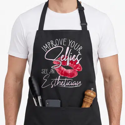Improve esthetician apron - Stacked white and pink text around a red lip print graphic — shown on a black cotton canvas apron against a white background