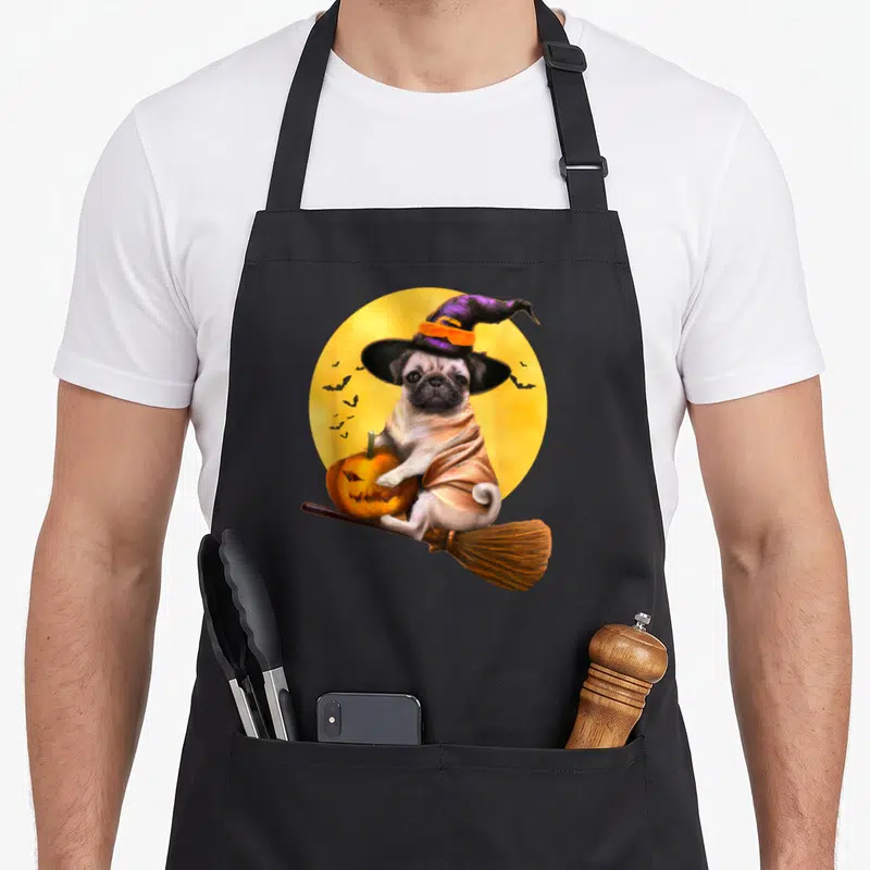 Pug costume cheap halloween aprons - Realistic pug in purple hat and cape riding broom with pumpkin against yellow moon — shown on a black cotton canvas apron against a white background